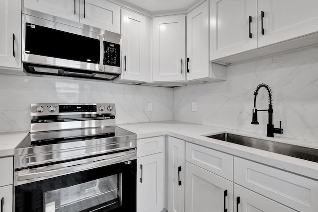 kitchen featuring stainless steel appliances, backsplash, a sink, and white cabinetry