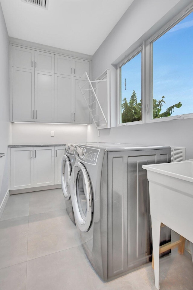 clothes washing area featuring cabinets, light tile patterned floors, and independent washer and dryer