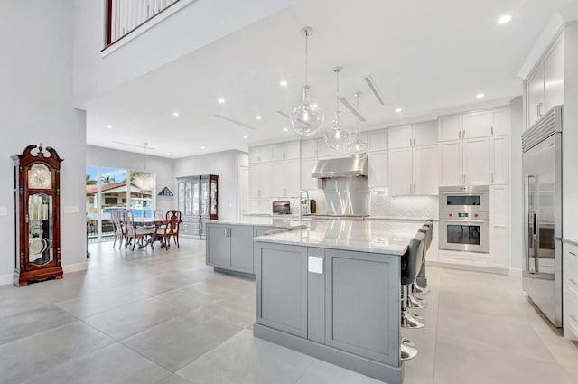 kitchen featuring a large island with sink, white cabinetry, tasteful backsplash, and pendant lighting