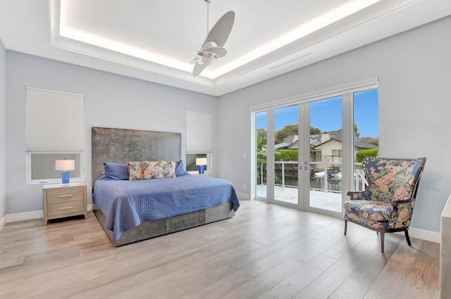 bedroom featuring ceiling fan, light hardwood / wood-style floors, french doors, access to outside, and a raised ceiling