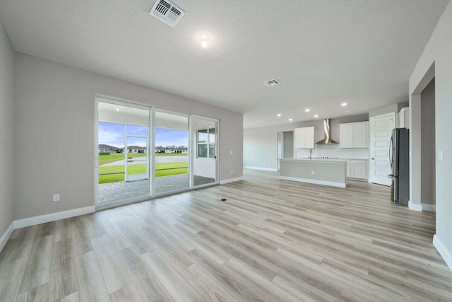 unfurnished living room featuring sink, a textured ceiling, and light wood-type flooring