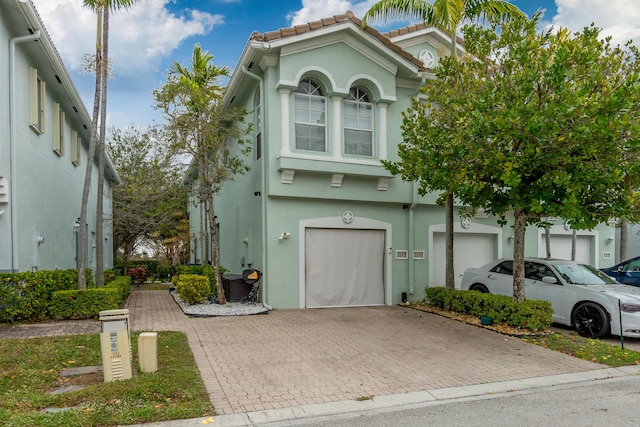 view of front of house with an attached garage, a tile roof, decorative driveway, and stucco siding