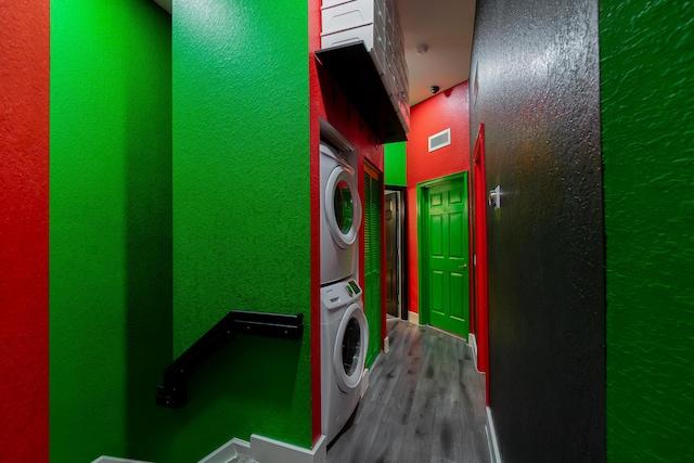 washroom with a textured wall, laundry area, wood finished floors, visible vents, and stacked washing maching and dryer