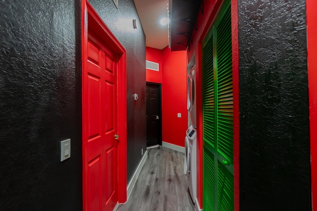 hallway featuring a textured wall, stacked washer / dryer, visible vents, baseboards, and light wood finished floors