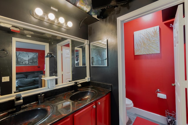 bathroom with toilet, double vanity, baseboards, and a sink