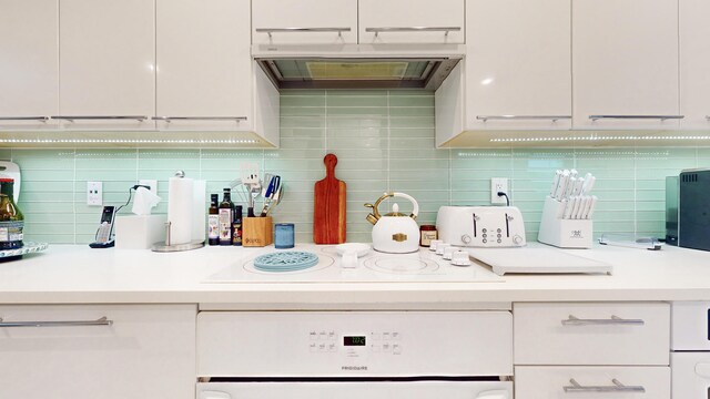 kitchen with extractor fan, white electric cooktop, white cabinets, decorative backsplash, and oven