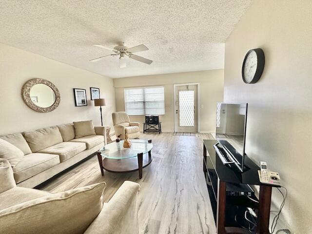 living room with hardwood / wood-style flooring, ceiling fan, and a textured ceiling