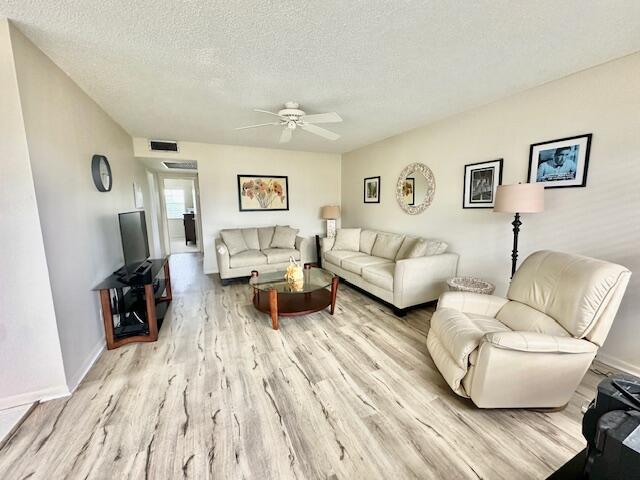 living room with ceiling fan, light hardwood / wood-style flooring, and a textured ceiling