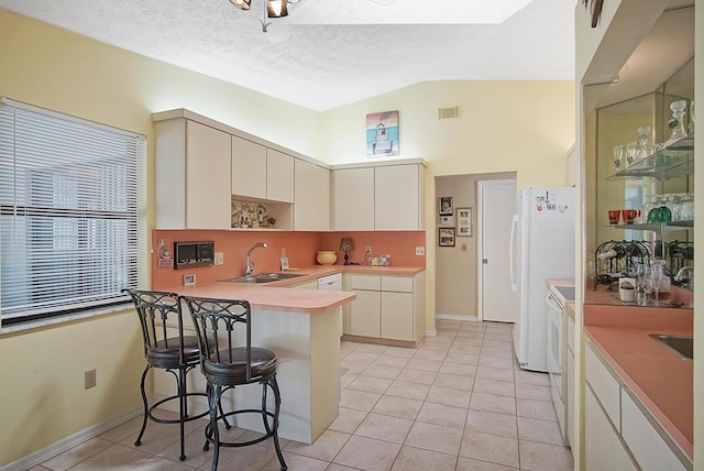 kitchen featuring sink, white appliances, a breakfast bar area, light tile patterned floors, and kitchen peninsula