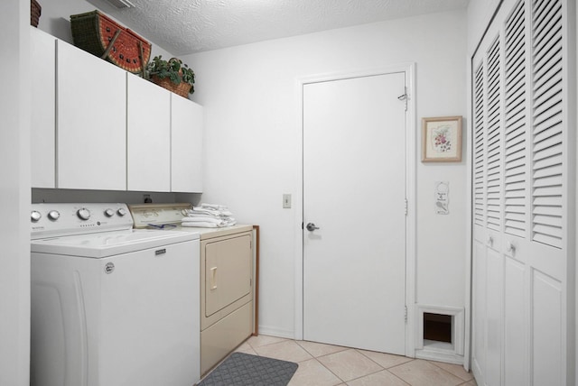 laundry area featuring light tile patterned floors, a textured ceiling, cabinets, and washing machine and clothes dryer