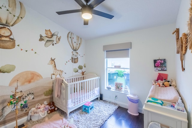 bedroom with a crib, dark hardwood / wood-style floors, and ceiling fan