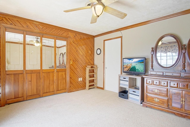 interior space with crown molding, light colored carpet, ceiling fan, and wood walls