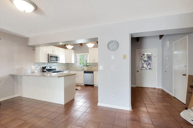 kitchen featuring dark tile patterned flooring, white cabinets, backsplash, kitchen peninsula, and stainless steel appliances