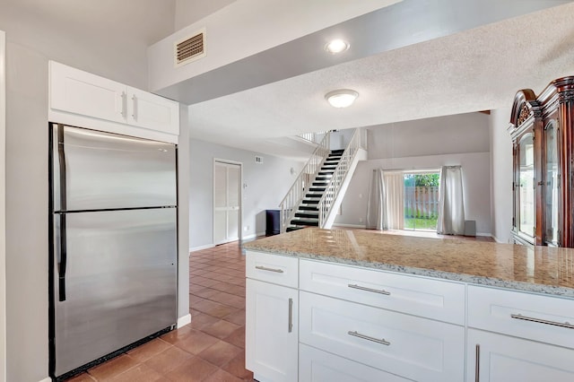 kitchen with light tile patterned floors, stainless steel fridge, white cabinetry, light stone counters, and a textured ceiling