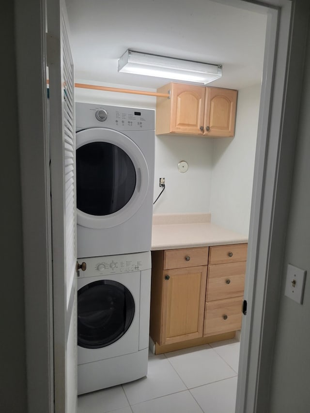 clothes washing area with stacked washer / drying machine, light tile patterned floors, and cabinets