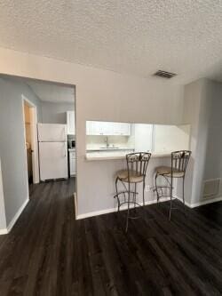 kitchen featuring dark wood-type flooring, a breakfast bar, kitchen peninsula, white fridge, and white cabinets