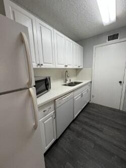 kitchen with dark hardwood / wood-style floors, white cabinetry, sink, white appliances, and a textured ceiling