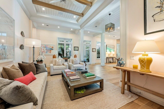 living room with a towering ceiling, decorative columns, beamed ceiling, crown molding, and light hardwood / wood-style flooring