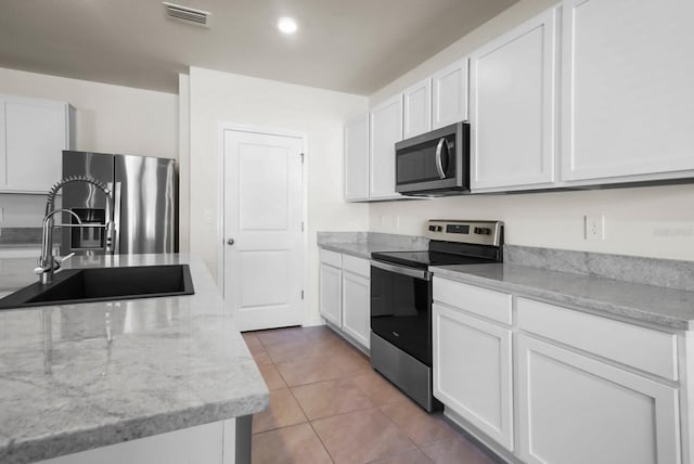 kitchen featuring sink, light tile patterned floors, stainless steel appliances, light stone countertops, and white cabinets