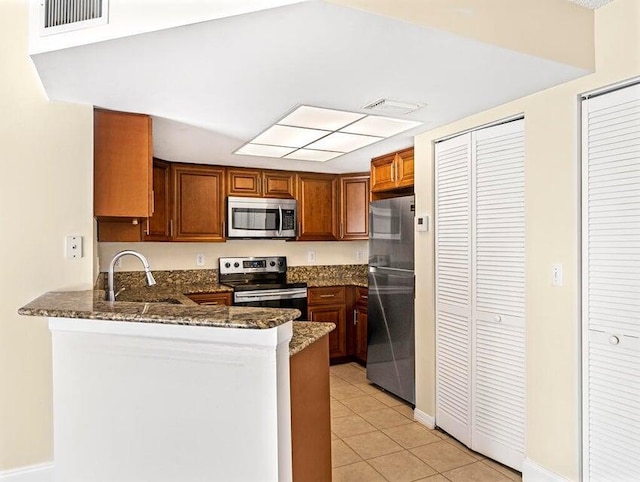 kitchen with stainless steel appliances, sink, dark stone counters, and kitchen peninsula