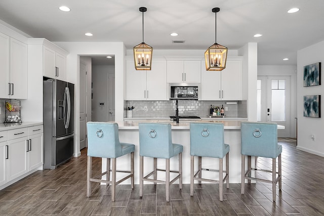 kitchen featuring white cabinetry, hanging light fixtures, a kitchen island with sink, and appliances with stainless steel finishes