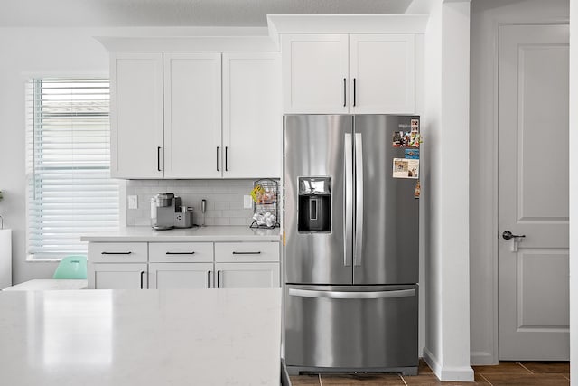 kitchen featuring stainless steel refrigerator with ice dispenser, white cabinetry, and backsplash