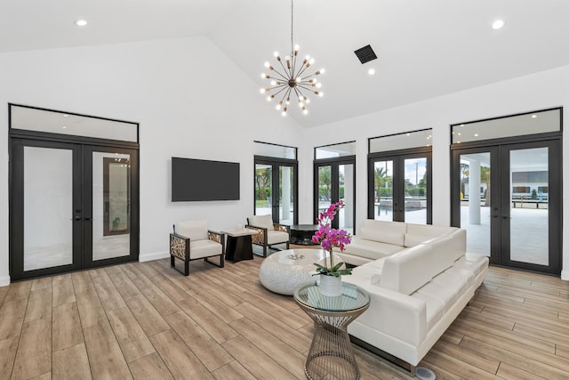 living room with plenty of natural light, a notable chandelier, high vaulted ceiling, and french doors