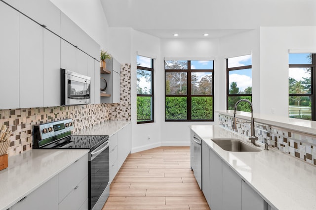 kitchen with sink, light hardwood / wood-style flooring, appliances with stainless steel finishes, white cabinetry, and tasteful backsplash