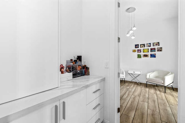 interior space featuring light stone counters, decorative light fixtures, light hardwood / wood-style floors, and white cabinets