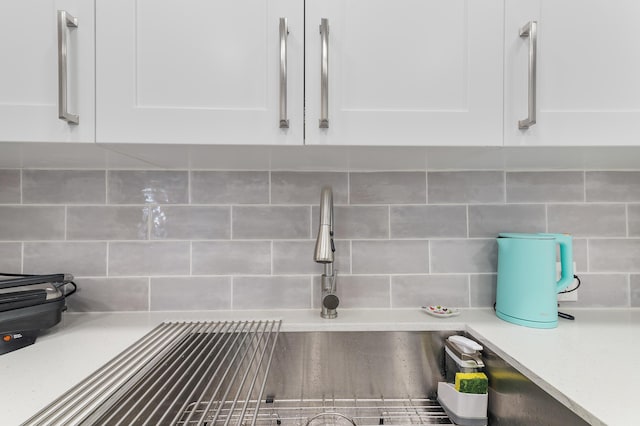 interior details featuring sink, decorative backsplash, and white cabinets