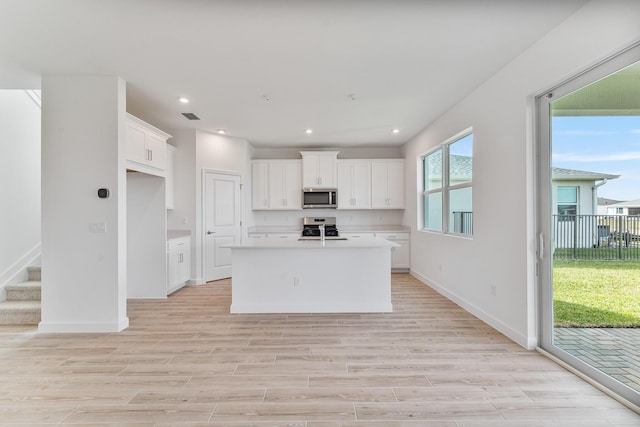 kitchen featuring white cabinetry, appliances with stainless steel finishes, light hardwood / wood-style floors, and a center island with sink