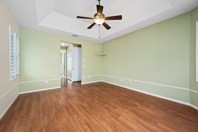 spare room with a tray ceiling, wood-type flooring, and ceiling fan