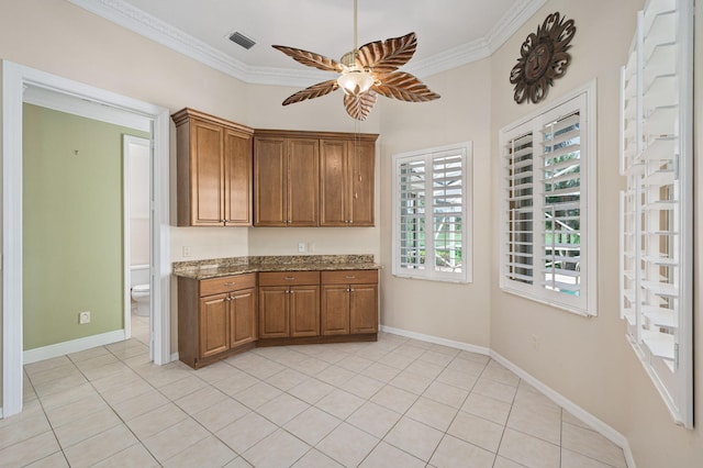 kitchen with light stone counters, ceiling fan, ornamental molding, and light tile patterned floors