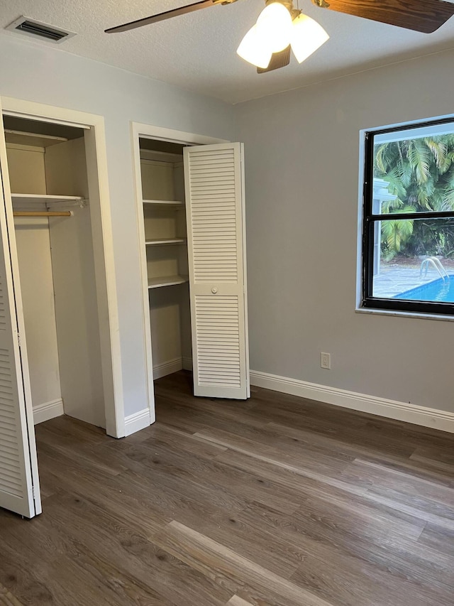 unfurnished bedroom featuring two closets, dark wood-type flooring, and ceiling fan