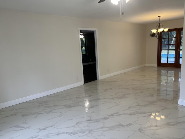 spare room featuring ceiling fan with notable chandelier and french doors