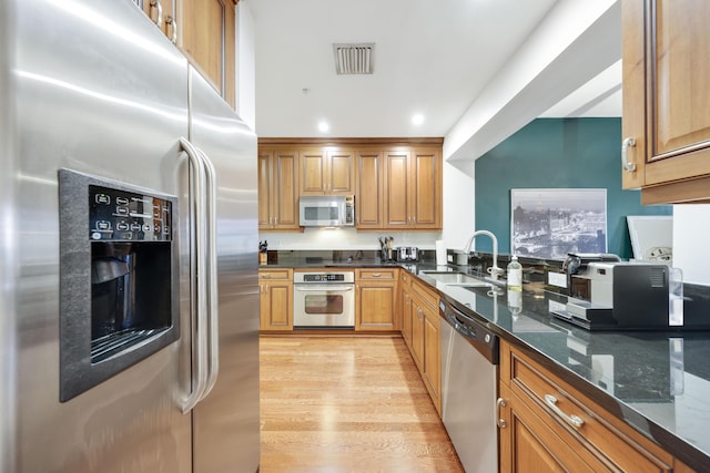 kitchen with dark stone countertops, sink, light hardwood / wood-style flooring, and stainless steel appliances