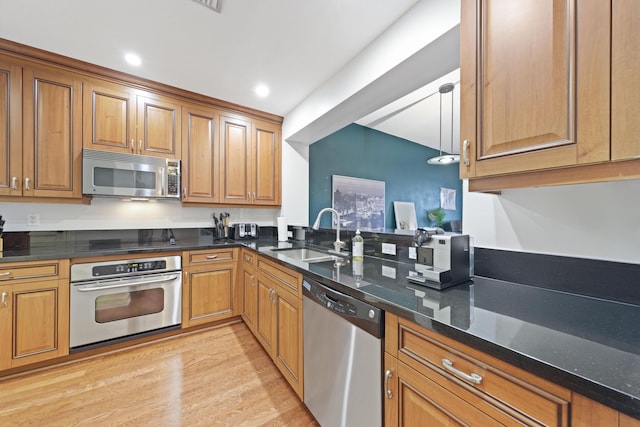 kitchen with sink, stainless steel appliances, dark stone counters, and light wood-type flooring