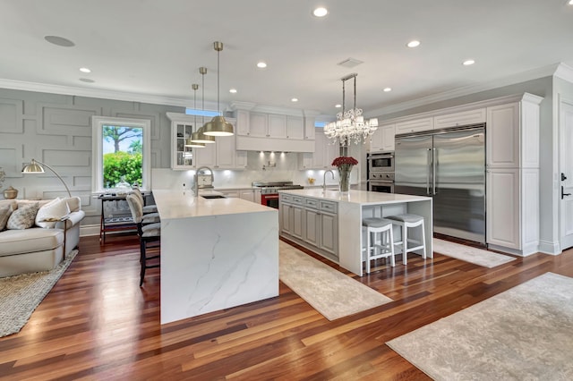 kitchen featuring decorative light fixtures, premium appliances, a kitchen breakfast bar, an island with sink, and white cabinets