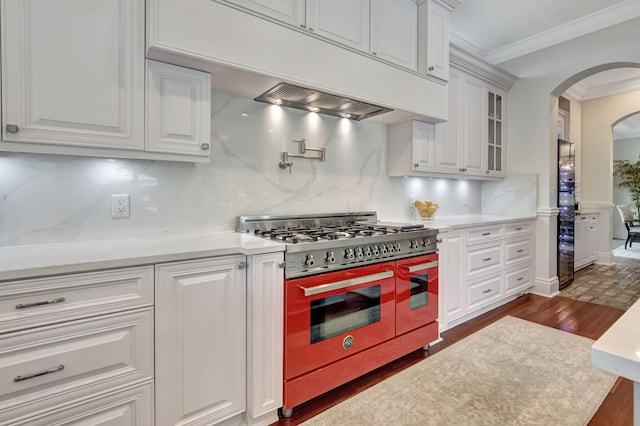 kitchen with white cabinetry, backsplash, range with two ovens, crown molding, and dark wood-type flooring