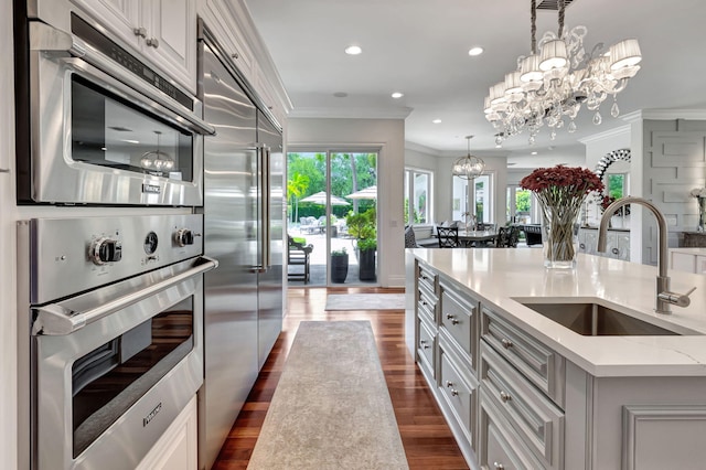 kitchen with white cabinetry, sink, hanging light fixtures, stainless steel built in fridge, and a center island with sink