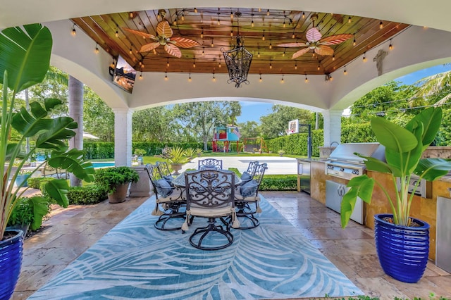 view of patio with a grill, ceiling fan, a playground, and an outdoor kitchen