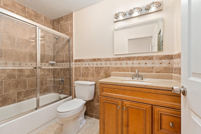 full bathroom featuring toilet, tile walls, a textured ceiling, vanity, and enclosed tub / shower combo