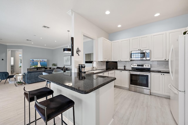 kitchen with appliances with stainless steel finishes, pendant lighting, sink, white cabinets, and kitchen peninsula