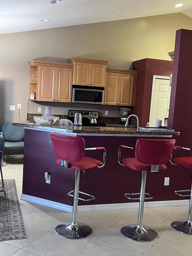 kitchen featuring light tile patterned flooring, appliances with stainless steel finishes, a breakfast bar area, and kitchen peninsula