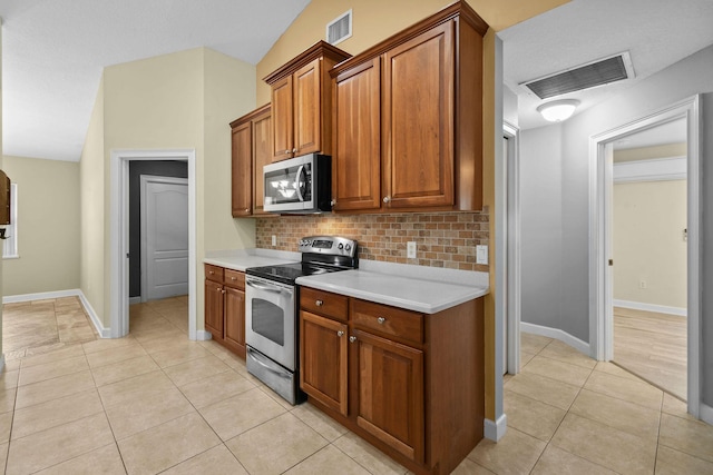 kitchen featuring lofted ceiling, light tile patterned floors, decorative backsplash, and stainless steel appliances