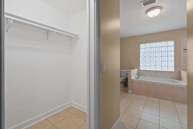 bathroom featuring a relaxing tiled tub, tile patterned floors, and toilet