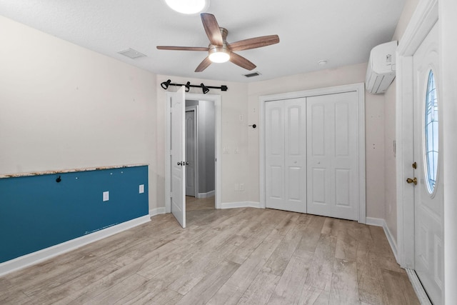 unfurnished bedroom featuring a wall mounted air conditioner, a closet, ceiling fan, a barn door, and light hardwood / wood-style flooring