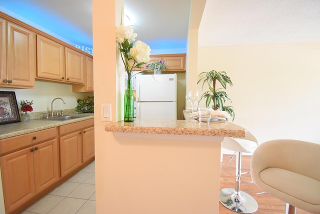 kitchen with white refrigerator, sink, light brown cabinetry, and a kitchen breakfast bar