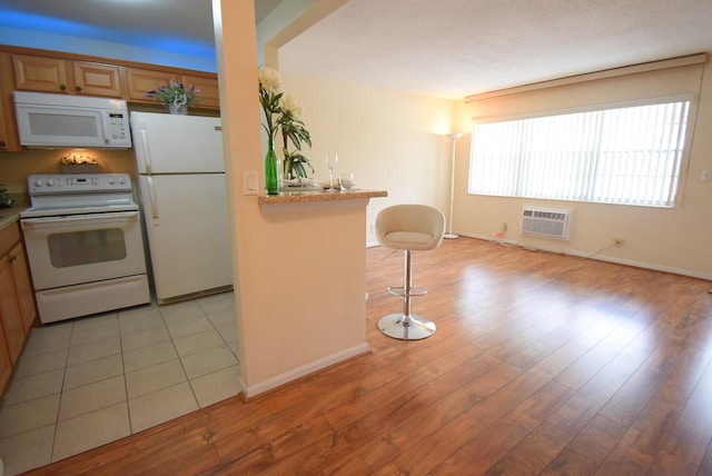 kitchen with white appliances, a wall mounted AC, light hardwood / wood-style floors, a kitchen bar, and kitchen peninsula