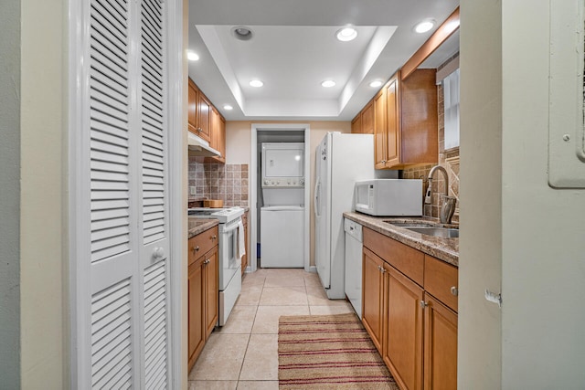 kitchen featuring sink, white appliances, stacked washer / drying machine, decorative backsplash, and a raised ceiling